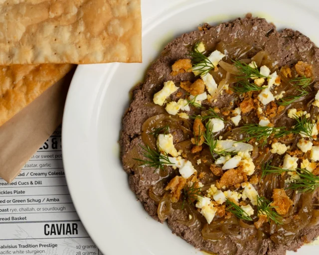 Maybe you grew up loving it. Maybe Bubbie’s version left you with some things to unpack. Either way, ours is worth another go.
Chopped Liver & Onions with gribenes and matzoh crackers. A little schmaltzy, a little crunchy, and maybe the one that changes your mind.